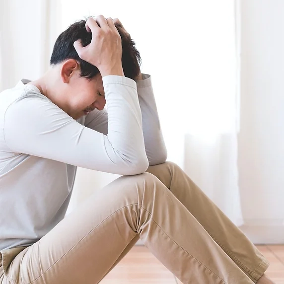 Depression Psychotherapie Wunstorf - Ein Mann der auf dem Boden sitzt und den Kopf in seinen Händen vergraben hat mit den Ellenbogen auf seinen Knien, Stress, Erschöpfung, Trauer Selbstzweifel